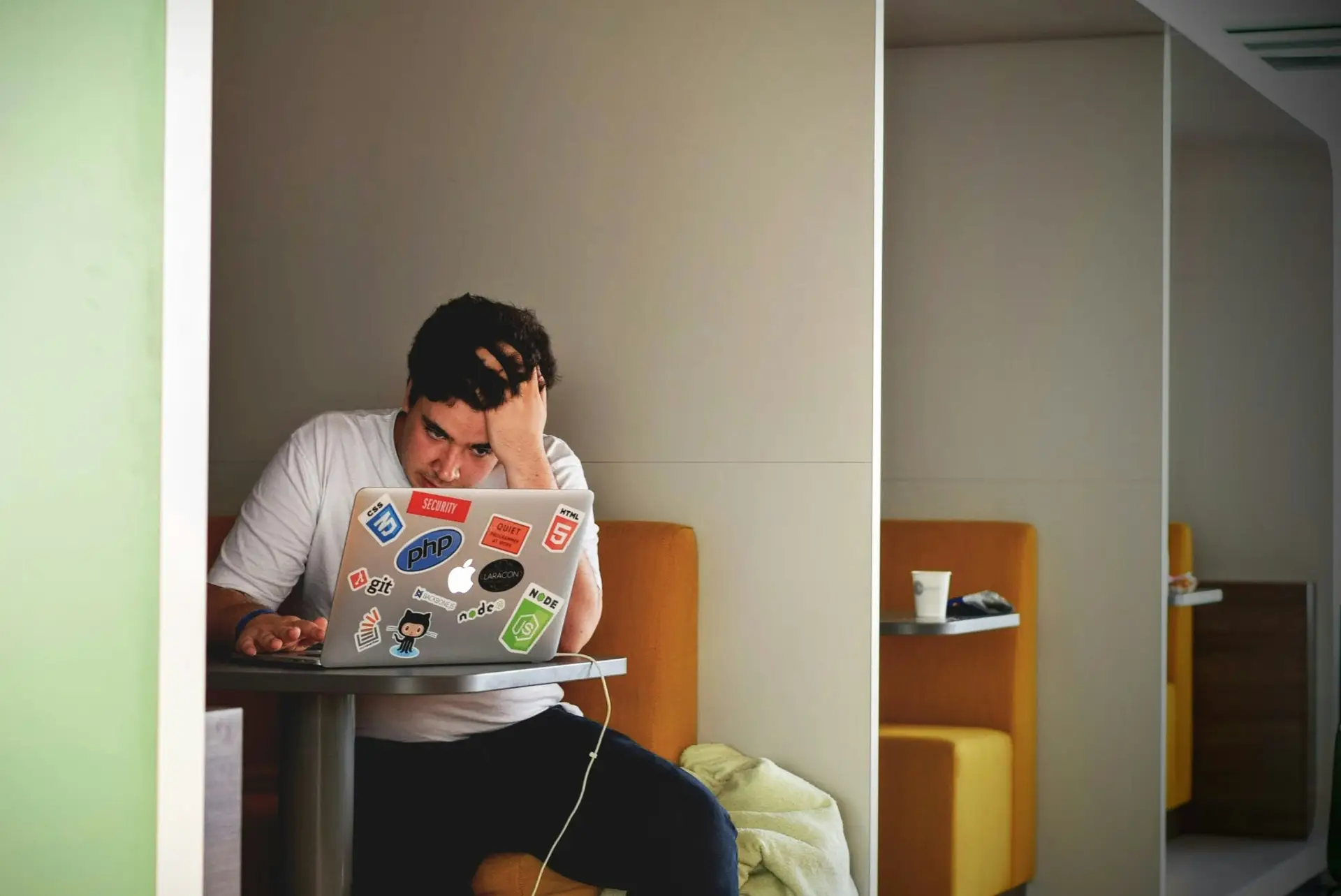 Man stressed and working on laptop with developer stickers while sitting in booth workspace