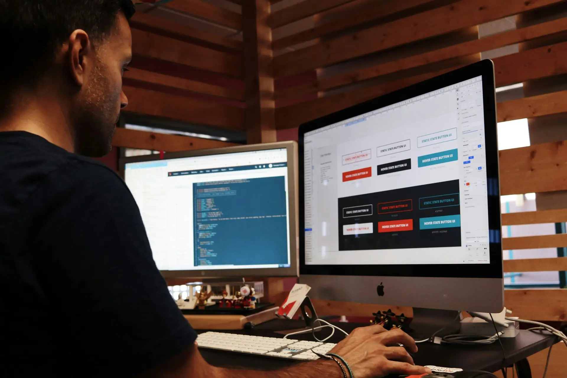 A UI/UX designer working in front of his two monitors displaying code and different button component styles